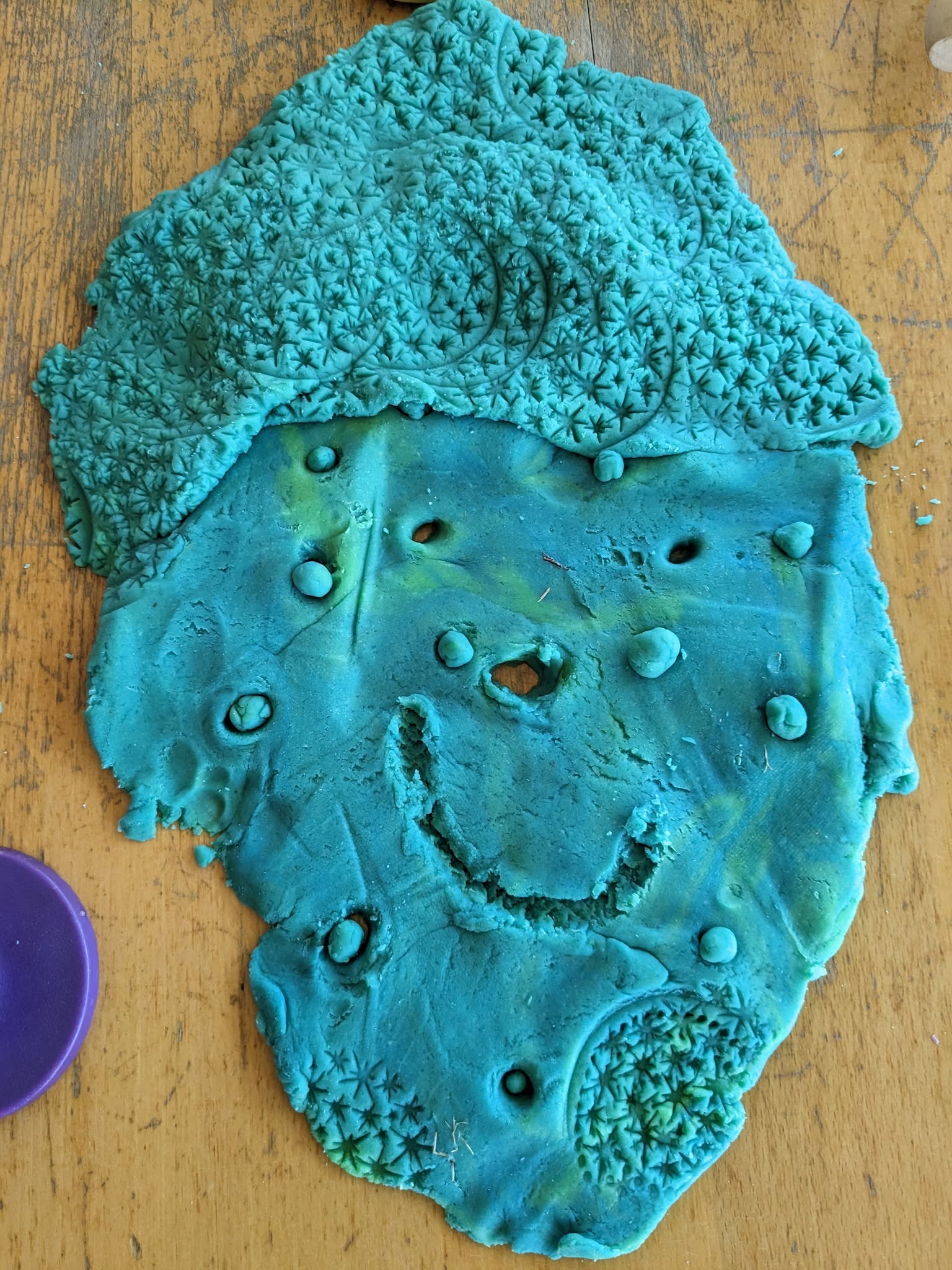 A child's playdough creation, patterned with stamps and textures